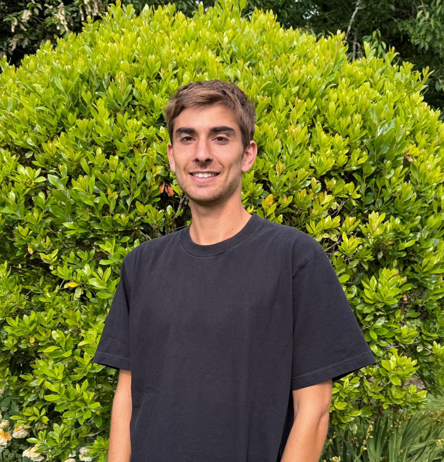 Jacob Simons standing outside in front of green foliage.